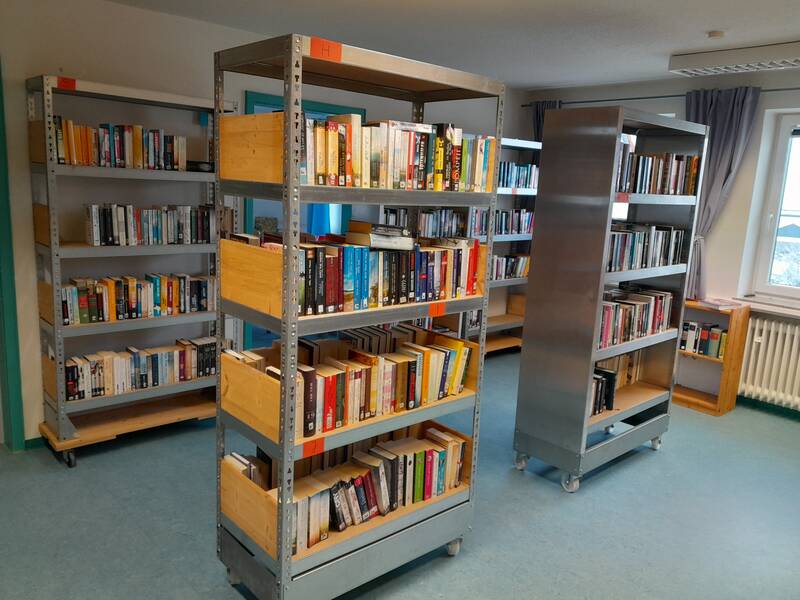 Das Bild zeigt einen Raum mit mehreren Metallbücheregalen auf Rollen, die mit verschiedenen Büchern gefüllt sind.