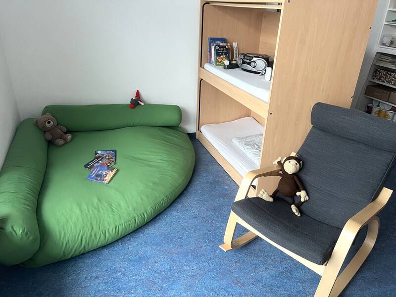 Ein gemütlicher Raum mit einem grünen Sitzsack, ein Regal mit zwei Schlafplätzen und Spielzeug sowie ein schwarzer Schaukelstuhl mit einem Stoffaffen darauf.